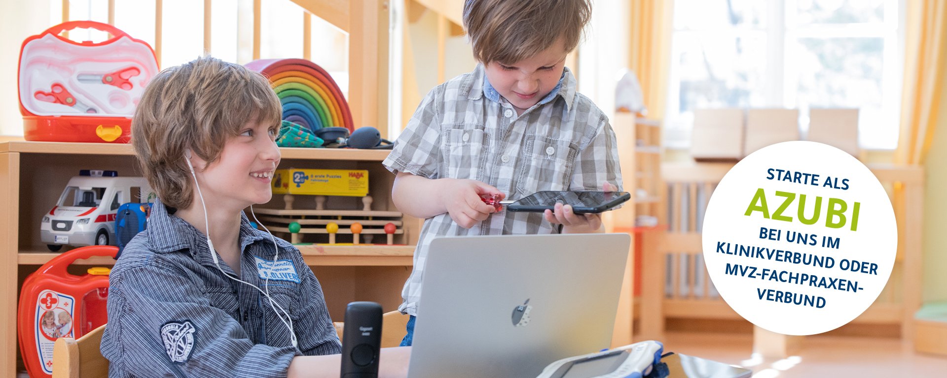 Zwei Kinder spielen als Erwachsene verkleidet mit einem PC. Im Hintergrund stehen medizinische Taschen und Koffer.